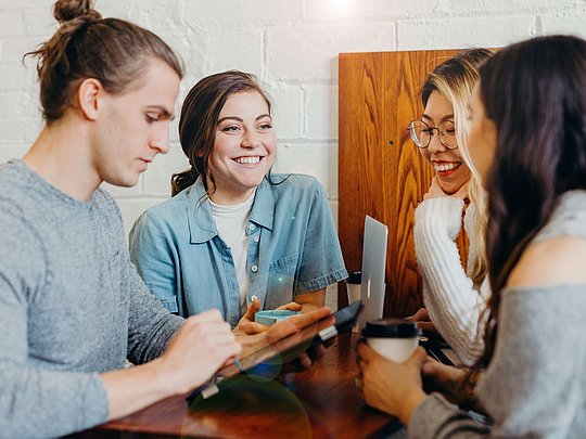 Drei Frauen und ein Mann unterhalten sich und lächeln