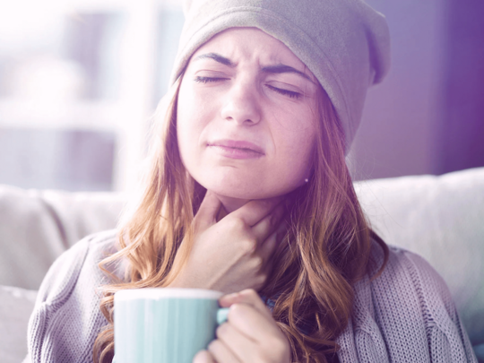 Frau greift sich mit der Hand an den Hals und hält Tasse in der Hand