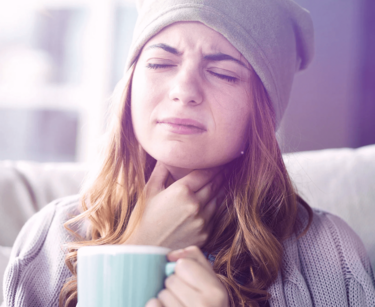 Frau greift sich mit der Hand an den Hals und hält Tasse in der Hand