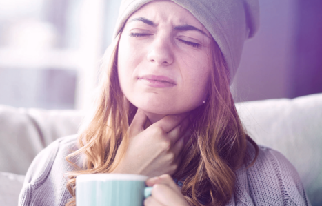 Frau greift sich mit der Hand an den Hals und hält Tasse in der Hand