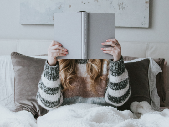 Frau sitzt im Bett mit einem Buch vor dem Gesicht