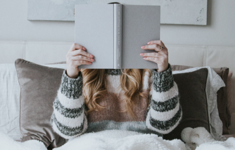 Frau sitzt im Bett mit einem Buch vor dem Gesicht